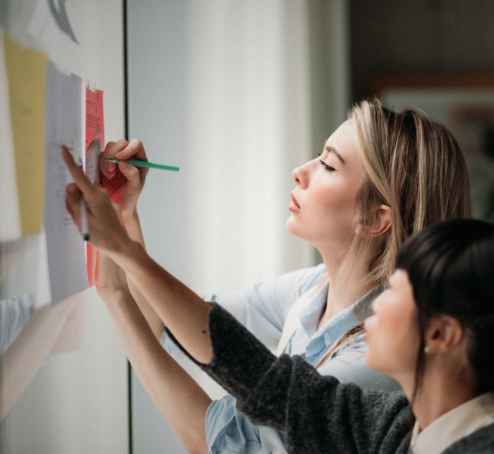 Zwei Frauen, die an einer Wand voller Post-Its arbeiten